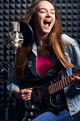 Image showing Girl musician in recording studio playing electric guitar and singing in mic