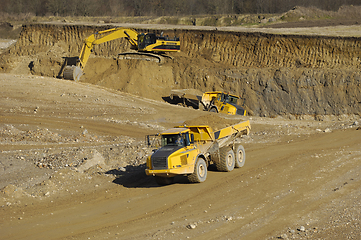 Image showing Yellow dump trucks and excavator are working in gravel pit