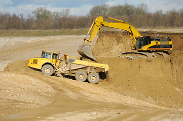 Image showing Yellow dump trucks and excavator are working in gravel pit