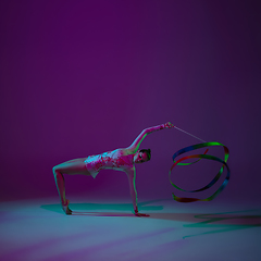 Image showing Young female athlete, rhythmic gymnastics artist on purple background with neon light. Beautiful girl practicing with equipment. Grace in performance.