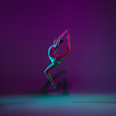 Image showing Young female athlete, rhythmic gymnastics artist on purple background with neon light. Beautiful girl practicing with equipment. Grace in performance.