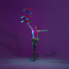 Image showing Young female athlete, rhythmic gymnastics artist on purple background with neon light. Beautiful girl practicing with equipment. Grace in performance.