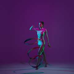 Image showing Young female athlete, rhythmic gymnastics artist on purple background with neon light. Beautiful girl practicing with equipment. Grace in performance.