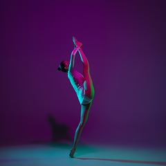 Image showing Young female athlete, rhythmic gymnastics artist on purple background with neon light. Beautiful girl practicing with equipment. Grace in performance.