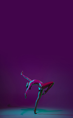 Image showing Young female athlete, rhythmic gymnastics artist on purple background with neon light. Beautiful girl practicing with equipment. Grace in performance.