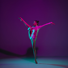 Image showing Young female athlete, rhythmic gymnastics artist on purple background with neon light. Beautiful girl practicing with equipment. Grace in performance.