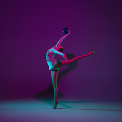 Image showing Young female athlete, rhythmic gymnastics artist on purple background with neon light. Beautiful girl practicing with equipment. Grace in performance.