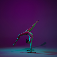 Image showing Young female athlete, rhythmic gymnastics artist on purple background with neon light. Beautiful girl practicing with equipment. Grace in performance.