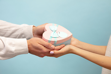 Image showing Close up hands of beautiful couple in love holding giftbox on blue studio background. Valentine\'s Day, love and emotions concept