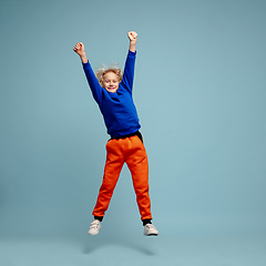 Image showing Happy curly boy isolated on blue studio background. Looks happy, cheerful, sincere. Copyspace. Childhood, education, emotions concept