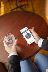 Image showing Close up hands holding smartphone with trading information graphs on the screen. Business, finance. Modern tech and work.