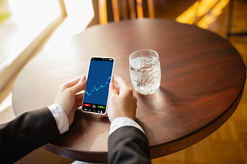 Image showing Close up hands holding smartphone with trading information graphs on the screen. Business, finance. Modern tech and work.