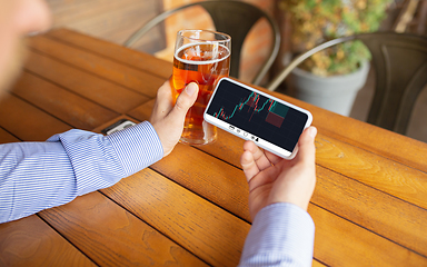 Image showing Close up hands holding smartphone with trading information graphs on the screen. Business, finance. Modern tech and work.