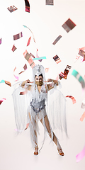 Image showing Beautiful young woman in carnival, stylish masquerade costume with feathers dancing on white studio background with shining confetti