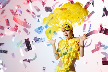 Image showing Beautiful young woman in carnival, stylish masquerade costume with feathers dancing on white studio background with shining confetti