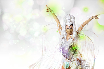 Image showing Beautiful young woman in carnival, stylish masquerade costume with feathers dancing on white studio background with shining bokeh