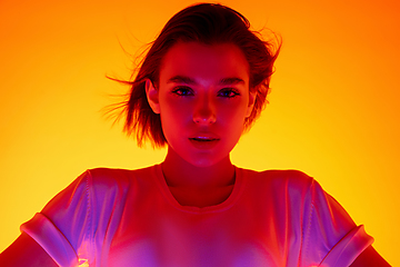 Image showing Caucasian woman\'s portrait isolated on orange studio background in multicolored neon light