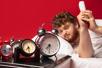 Image showing Man wakes up and he\'s mad at clock ringing, switches it off with rolled documents