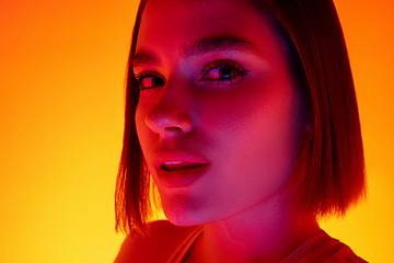 Image showing Caucasian woman\'s portrait isolated on orange studio background in multicolored neon light