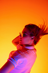 Image showing Caucasian woman\'s portrait isolated on orange studio background in multicolored neon light