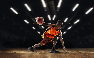 Image showing African-american young basketball player in action and flashlights over gym background. Concept of sport, movement, energy and dynamic, healthy lifestyle.