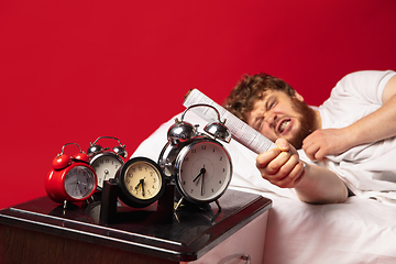 Image showing Man wakes up and he\'s mad at clock ringing, switches it off with rolled documents