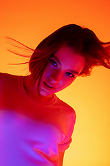 Image showing Caucasian woman\'s portrait isolated on orange studio background in multicolored neon light