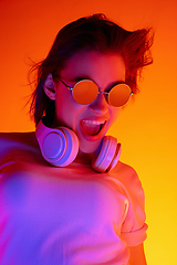 Image showing Caucasian woman\'s portrait isolated on orange studio background in multicolored neon light