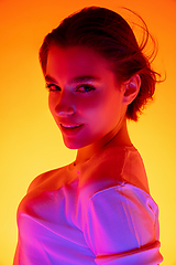 Image showing Caucasian woman\'s portrait isolated on orange studio background in multicolored neon light