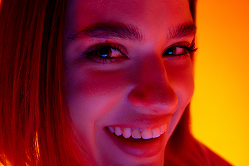 Image showing Caucasian woman\'s portrait isolated on orange studio background in multicolored neon light