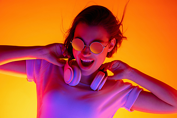 Image showing Caucasian woman\'s portrait isolated on orange studio background in multicolored neon light