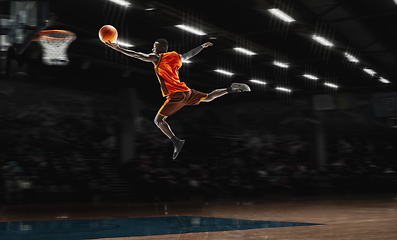 Image showing African-american young basketball player in action and flashlights over gym background. Concept of sport, movement, energy and dynamic, healthy lifestyle.