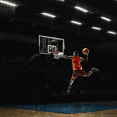 Image showing African-american young basketball player in action and flashlights over gym background. Concept of sport, movement, energy and dynamic, healthy lifestyle.