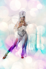 Image showing Beautiful young woman in carnival, stylish masquerade costume with feathers dancing on white studio background with shining bokeh