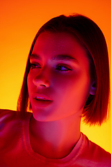 Image showing Caucasian woman\'s portrait isolated on orange studio background in multicolored neon light