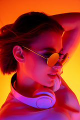 Image showing Caucasian woman\'s portrait isolated on orange studio background in multicolored neon light