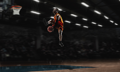 Image showing African-american young basketball player in action and flashlights over gym background. Concept of sport, movement, energy and dynamic, healthy lifestyle.