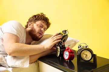 Image showing Man wakes up and he\'s mad at clock ringing, trying to switch it off, looks sleepy