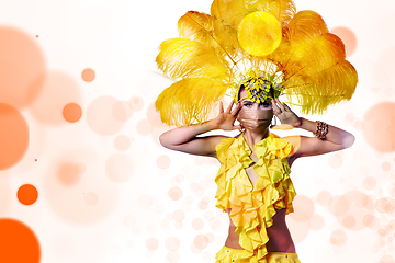 Image showing Beautiful young woman in carnival, stylish masquerade costume with feathers dancing on white studio background with shining bokeh