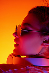 Image showing Caucasian woman\'s portrait isolated on orange studio background in multicolored neon light