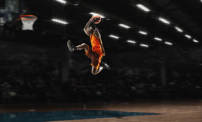 Image showing African-american young basketball player in action and flashlights over gym background. Concept of sport, movement, energy and dynamic, healthy lifestyle.