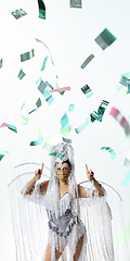 Image showing Beautiful young woman in carnival, stylish masquerade costume with feathers dancing on white studio background with shining confetti