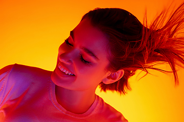 Image showing Caucasian woman\'s portrait isolated on orange studio background in multicolored neon light