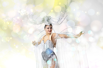 Image showing Beautiful young woman in carnival, stylish masquerade costume with feathers dancing on white studio background with shining confetti