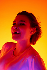 Image showing Caucasian woman\'s portrait isolated on orange studio background in multicolored neon light