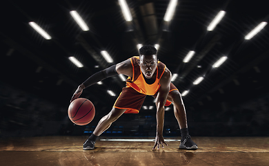 Image showing African-american young basketball player in action and flashlights over gym background. Concept of sport, movement, energy and dynamic, healthy lifestyle.