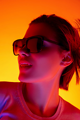Image showing Caucasian woman\'s portrait isolated on orange studio background in multicolored neon light