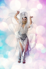 Image showing Beautiful young woman in carnival, stylish masquerade costume with feathers dancing on white studio background with shining bokeh