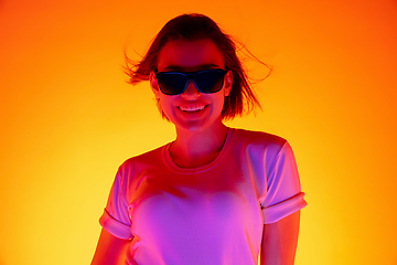 Image showing Caucasian woman\'s portrait isolated on orange studio background in multicolored neon light