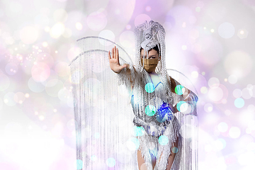 Image showing Beautiful young woman in carnival, stylish masquerade costume with feathers dancing on white studio background with shining bokeh
